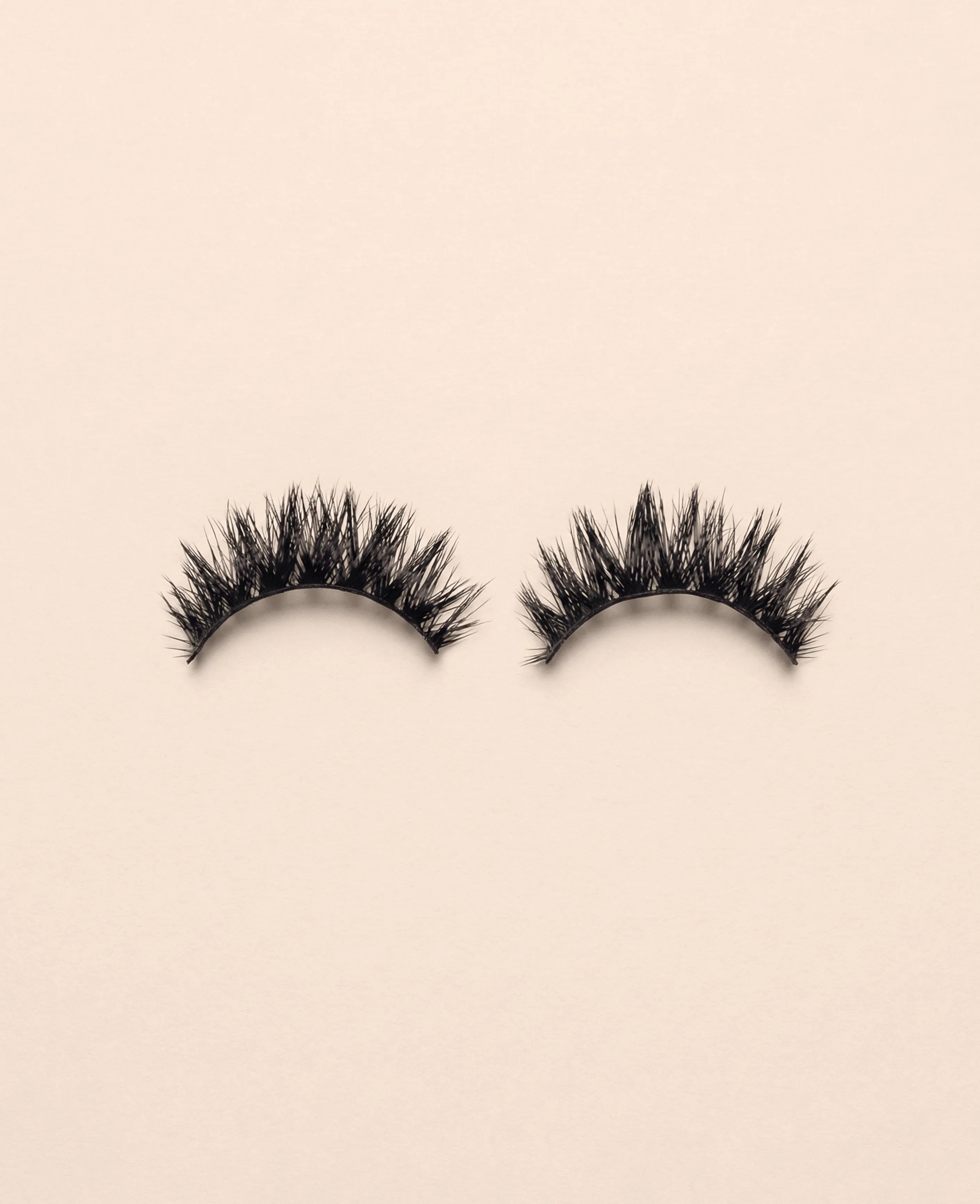 Pair of Amplify false eyelashes on a beige background.