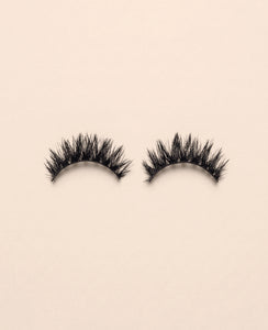 Pair of Amplify false eyelashes on a beige background.