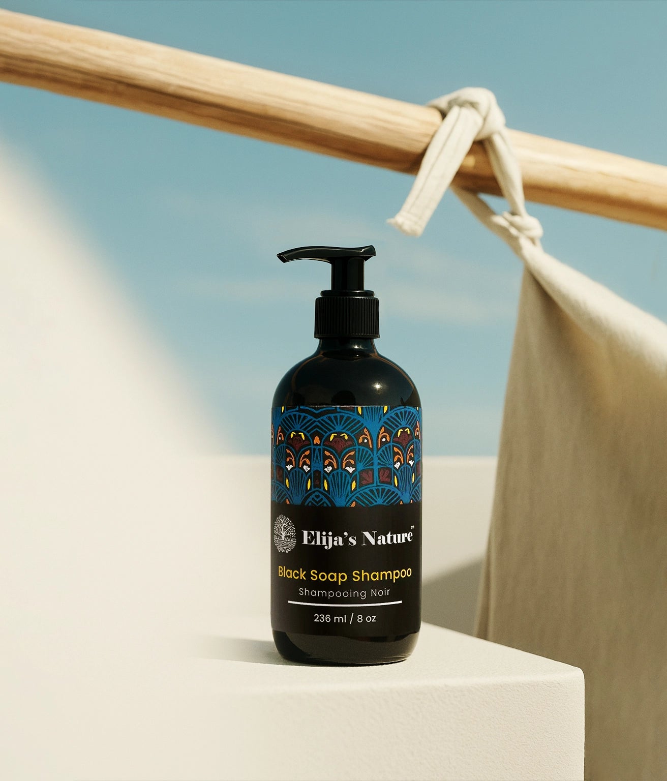 Black Soap Shampoo – #size_8oz - Bottle of Elija’s Nature Black Soap Shampoo on a white platform with draped fabric and a calm seascape in the background