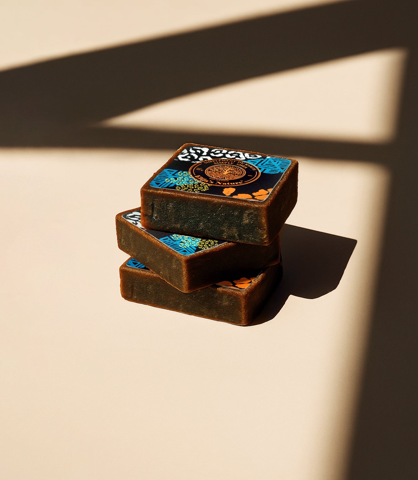 Stack of three Elija’s Nature Black Soap Bars with patterned labels, arranged on a beige surface with bold shadow lines