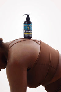 Black Soap Shampoo – #size_8oz - Elija’s Nature Black Soap Shampoo bottle balanced on a woman’s back as she leans forward, wearing a brown sports bra, set against a minimal white background