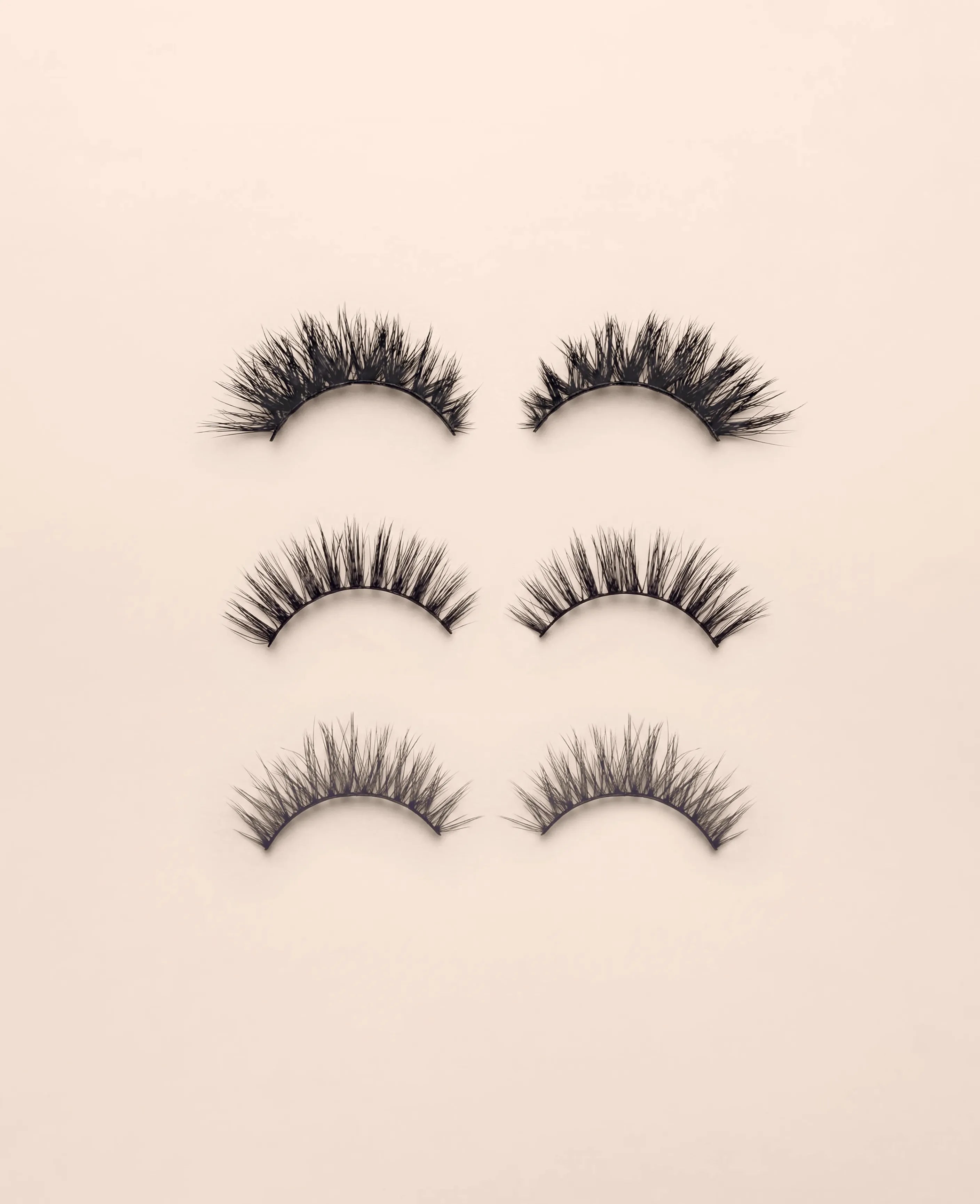 Set of three pairs of black false eyelashes on a beige background.