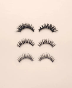 Set of three pairs of black false eyelashes on a beige background.