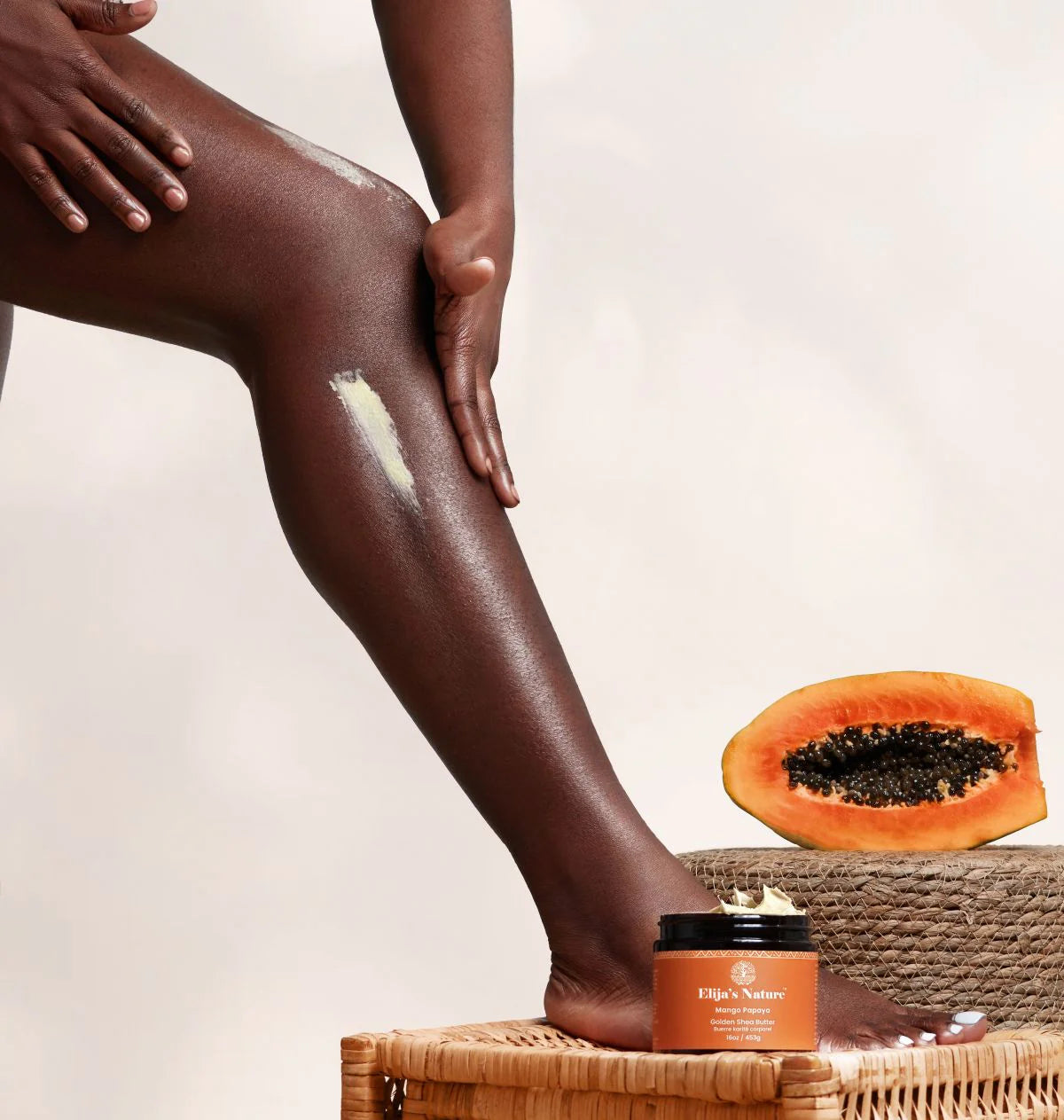 Golden Body Butter - #scent_Mango Papaya  #size_16oz - Woman applying body butter to her leg next to a papaya and Elija’s Nature product