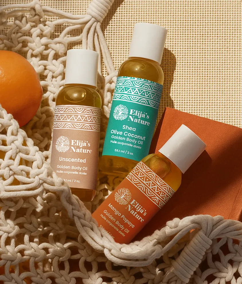 Heavenly Trio Gift Set - #size_2oz - Three Elija’s Nature body oil bottles: Unscented, Olive Coconut, and Mango Papaya placed in a woven bag with an orange on a warm-toned surface