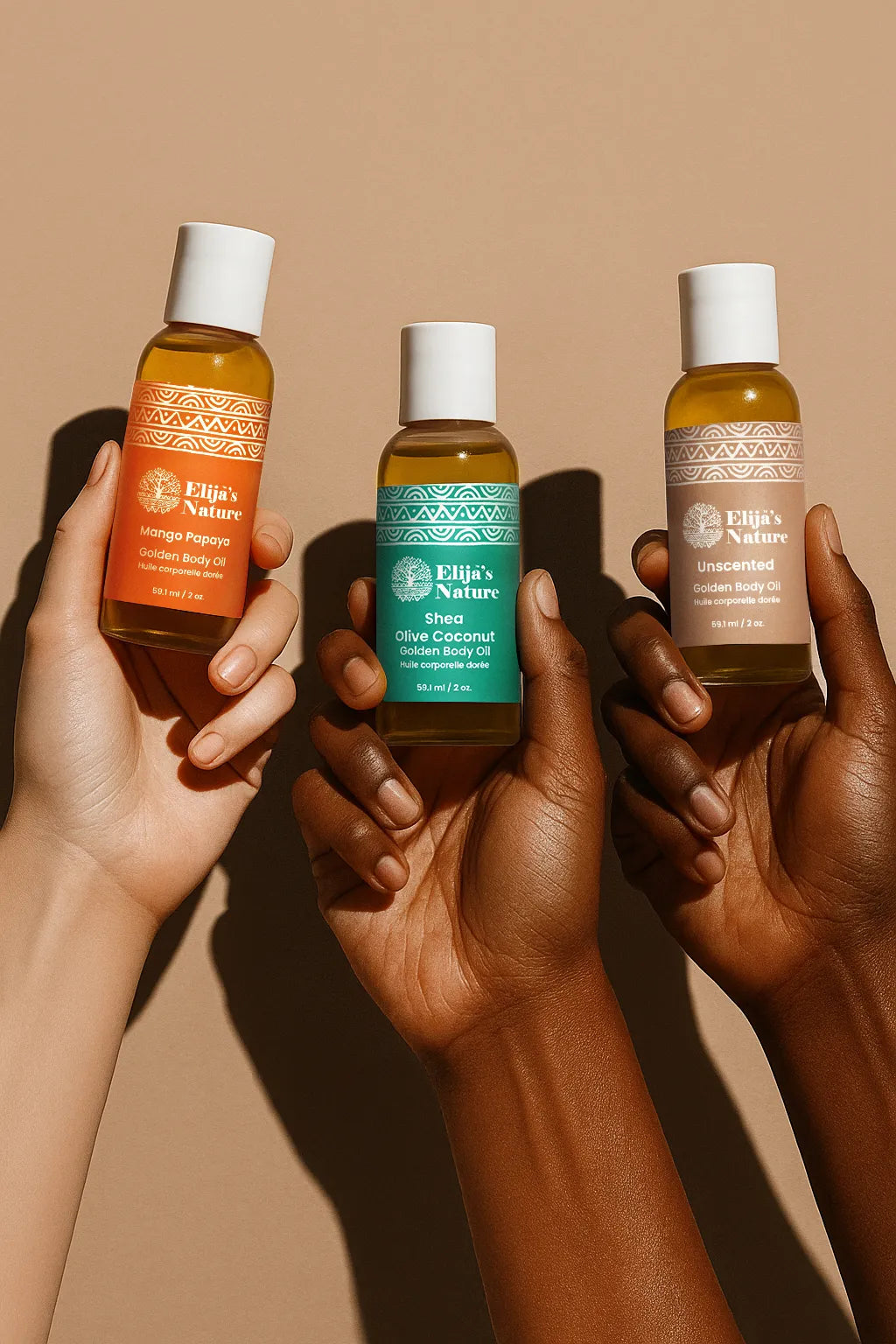 Heavenly Trio Gift Set - #size_2oz - Three hands of different skin tones holding Elija’s Nature mini body oils: Mango Papaya, Olive Coconut, and Unscented against a beige backdrop