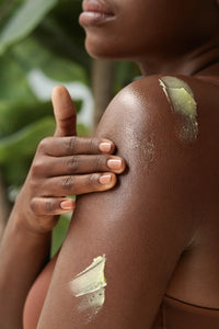Golden Body Butter - #scent_Lemon Blossom - A close-up of a woman gently applying a yellow-tinted body butter to her shoulder, suggesting targeted nourishment and a botanical formula
