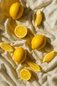 #scent_Lemon Blossom - Scattered fresh lemons and lemon halves arranged on soft beige fabric to evoke a bright citrus scent