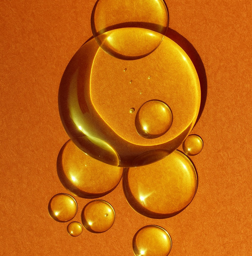 Close-up of golden oil drops on an orange background representing Elija’s Nature Golden Body Oil