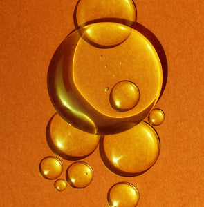 Close-up of golden oil drops on an orange background representing Elija’s Nature Golden Body Oil