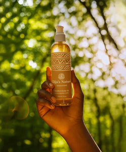 Golden Body Oil - #scent_Unscented #size_8oz - Hand holding a bottle of Elija’s Nature Unscented Golden Body Oil against a sun-dappled forest background
